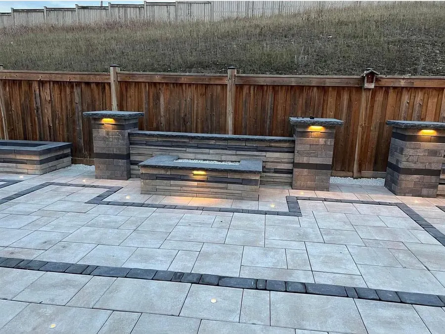 Backyard patio with built-in seat walls, fire feature and pillar lighting at dusk