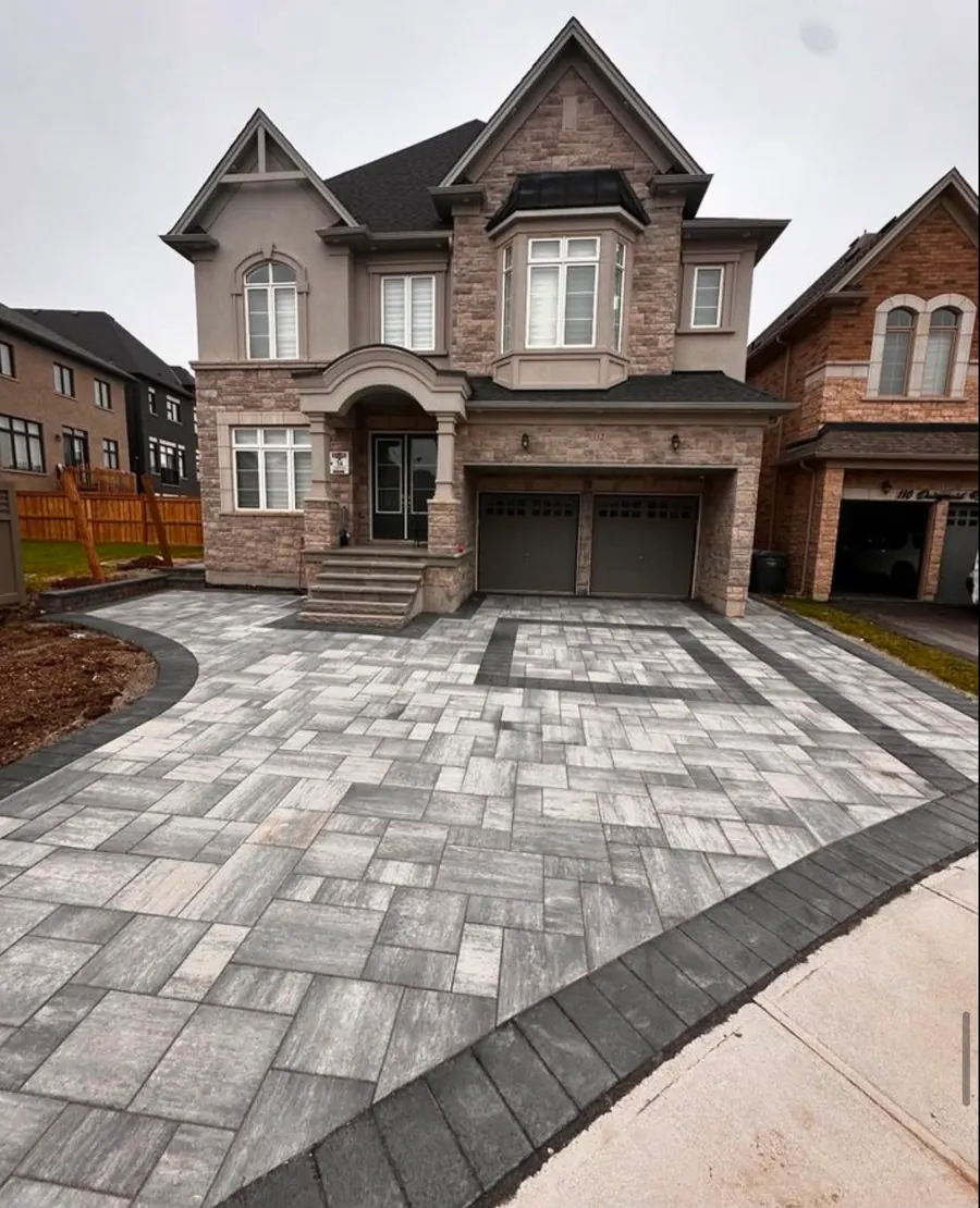Two-tone interlocking paver driveway in front of a stone-brick home