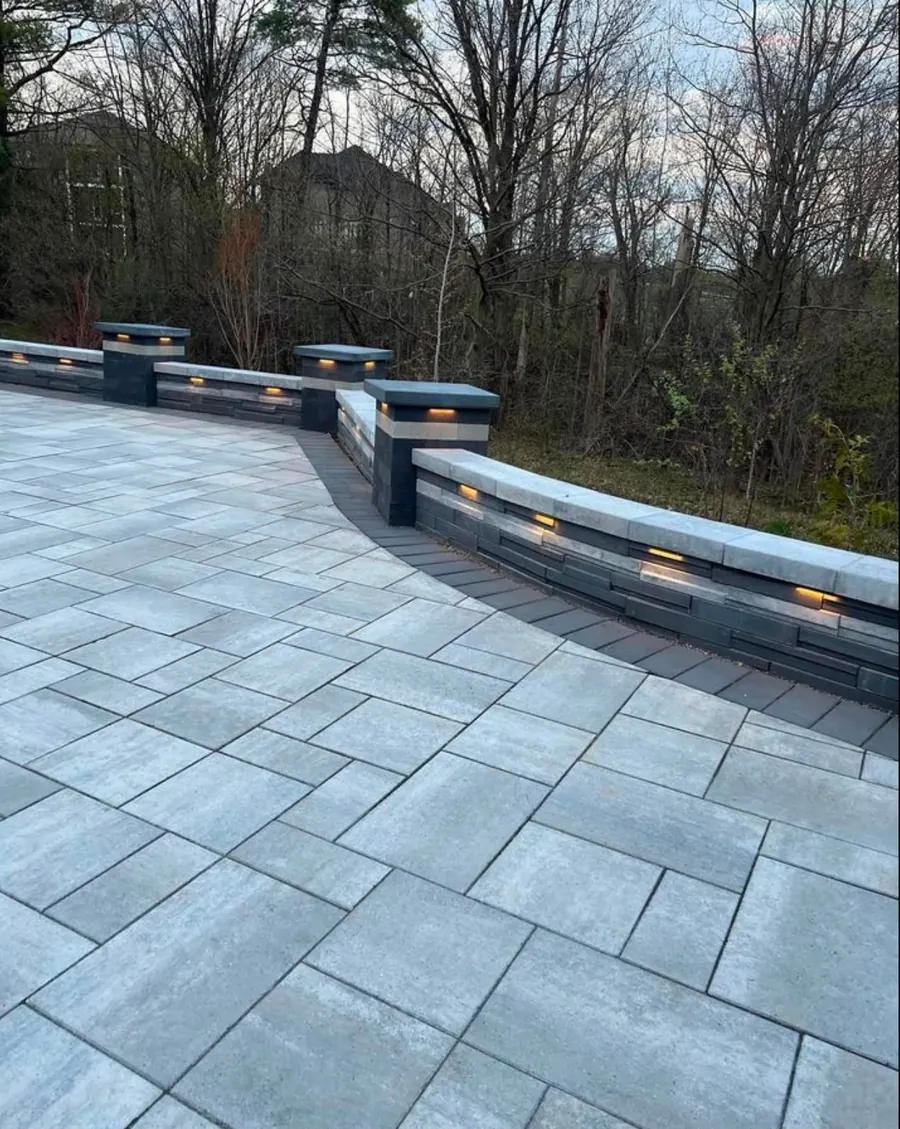 Curved illuminated seat wall running along a paver patio