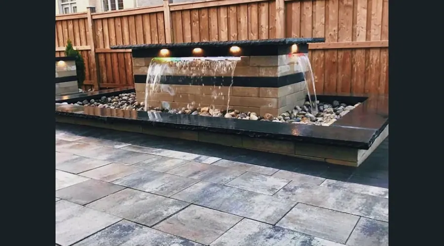Custom black granite water fountain feature with a river-rock bed
