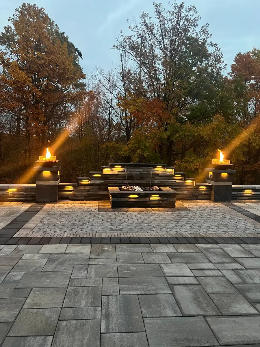 Fire pit patio with lit torches and a water feature at dusk