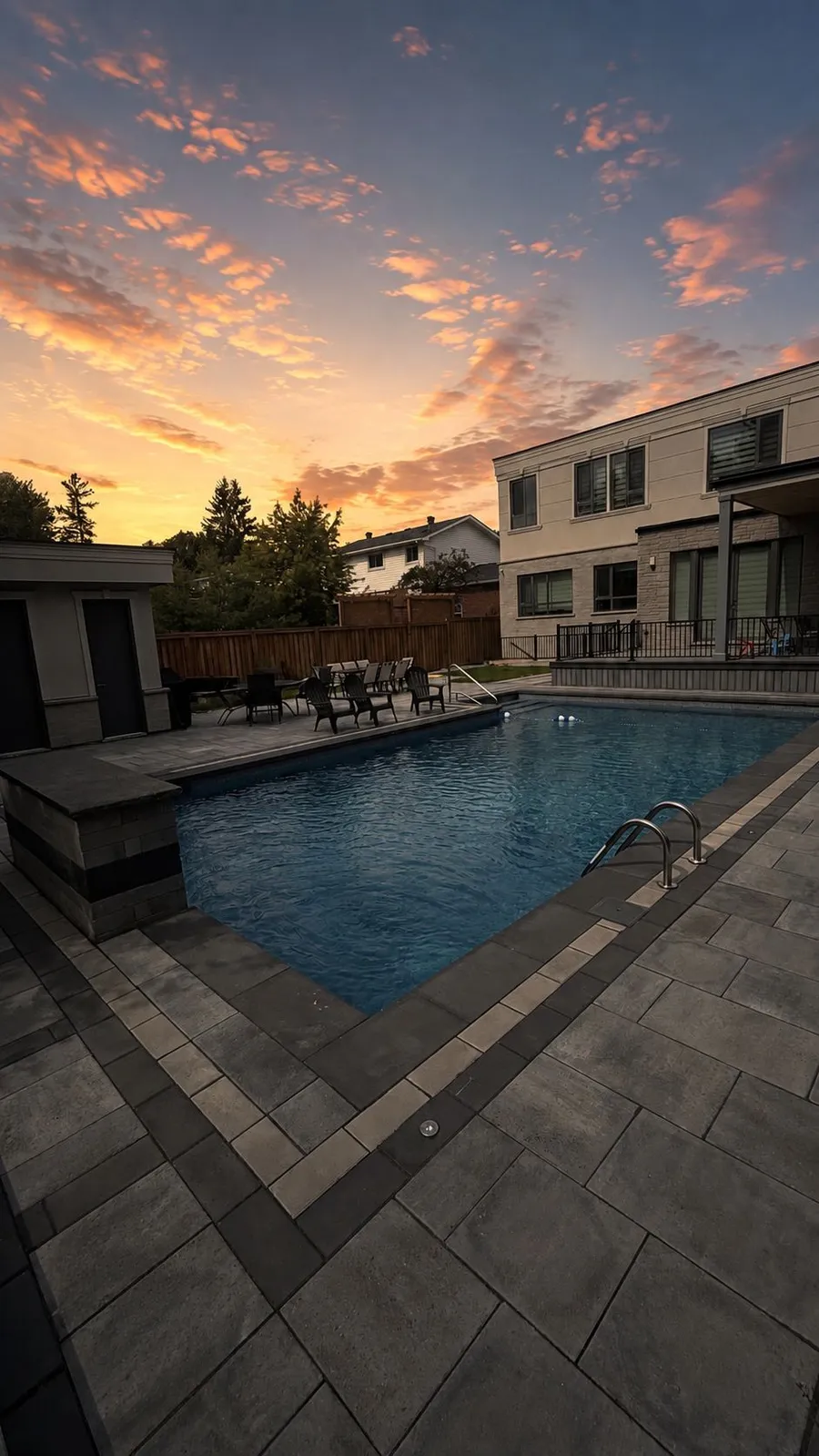 Wide paver pool deck with in-deck lighting wrapping a rectangular pool at dusk