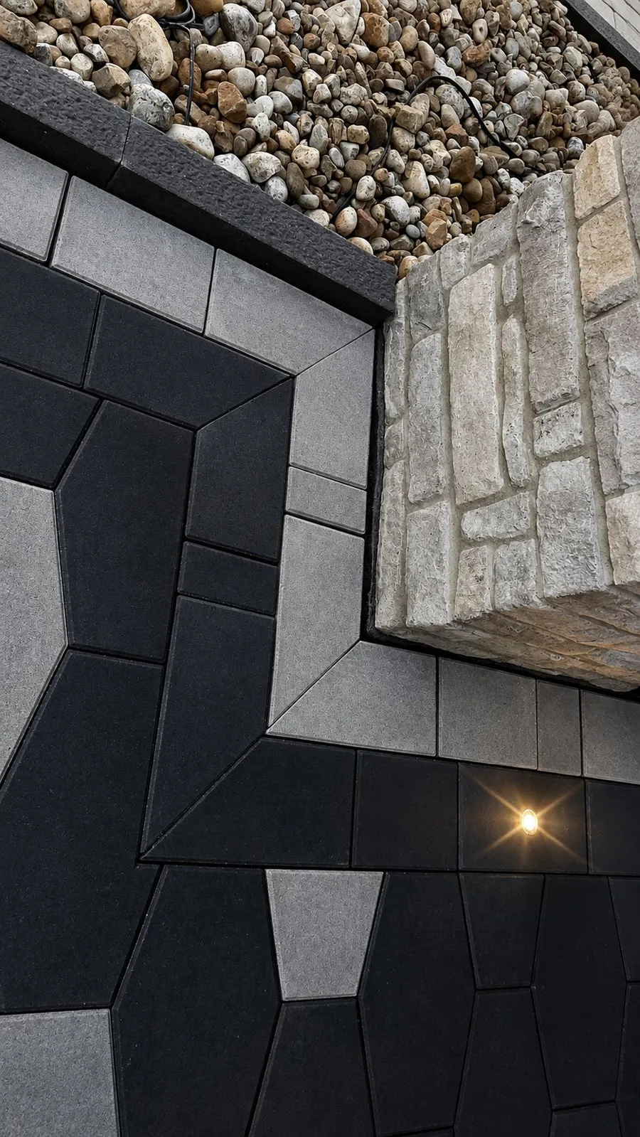 Close-up of black and grey paver banding with river rock and a recessed ground light