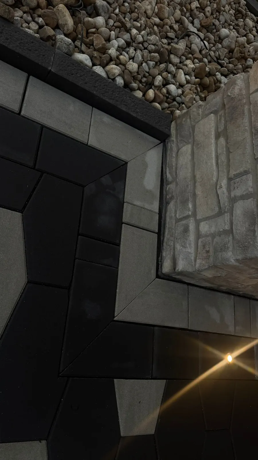 Detail of dark paver border patterns meeting a stone pillar and river-rock bed