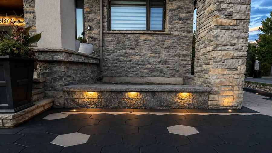 Front porch with stone pillars, a lit sitting wall and hexagon paver landing at dusk